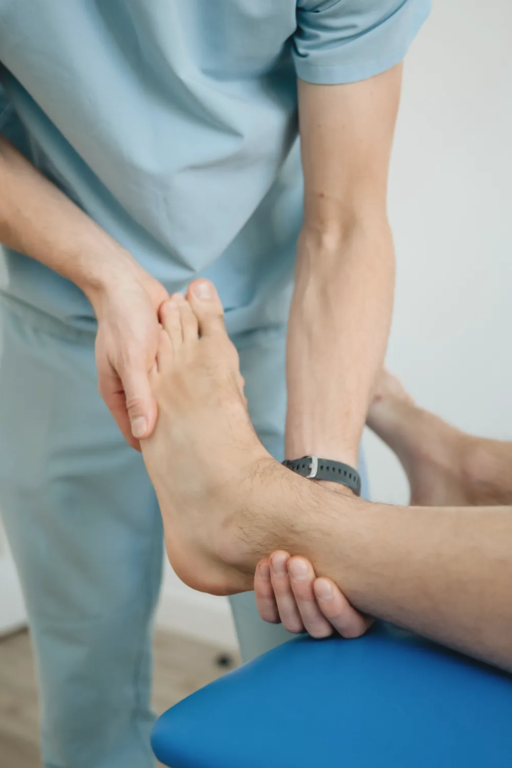 A clinician's hands support a patient's bare foot and ankle during an exam